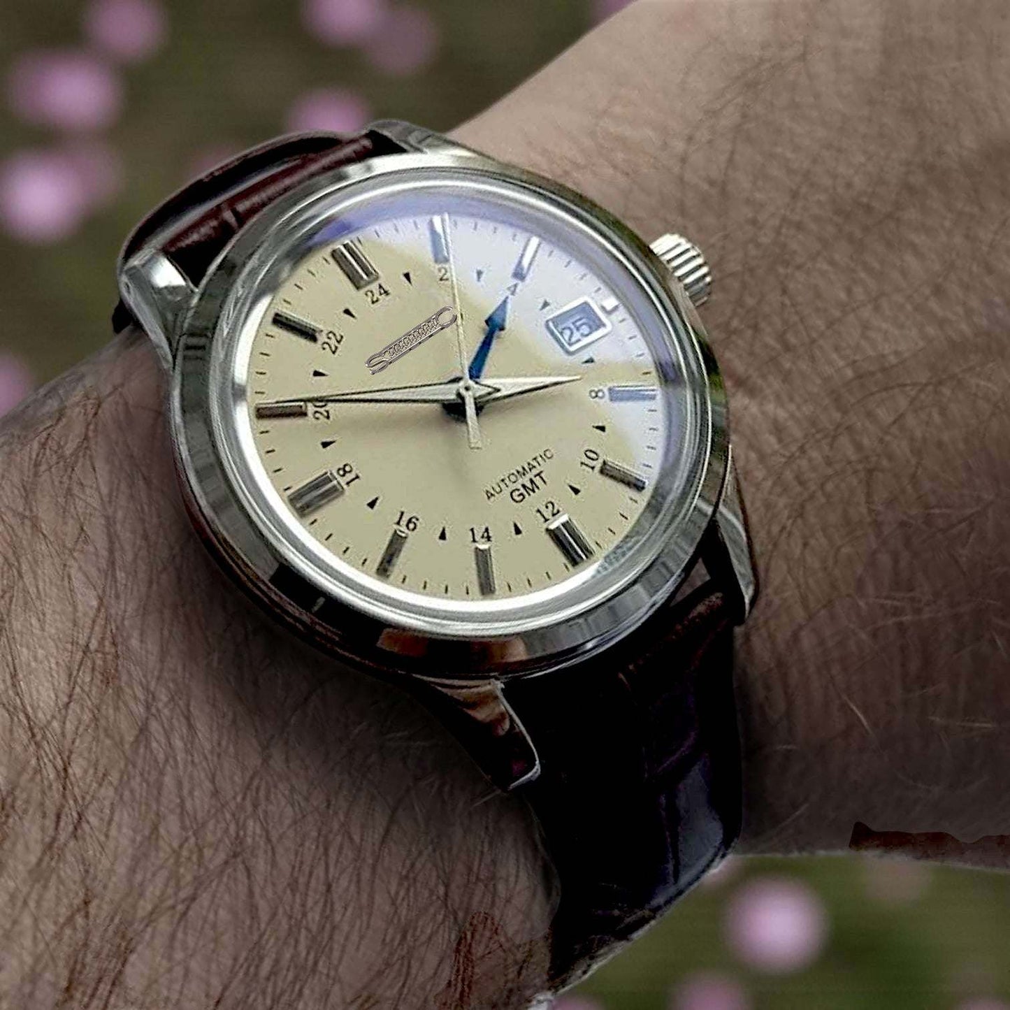 MODTIME GMT pilot mod watch with a cream dial, blue GMT hand, and brown leather strap worn on a wrist.