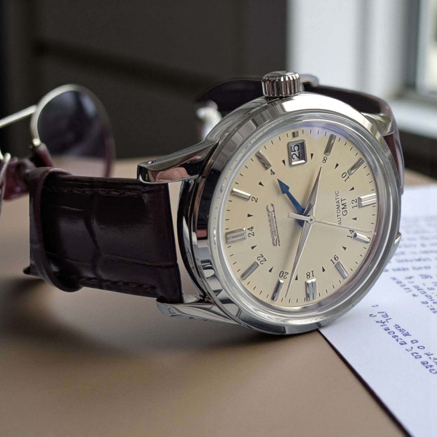 MODTIME GMT pilot mod watch with a cream dial, blue GMT hand, and brown leather strap on a desk.