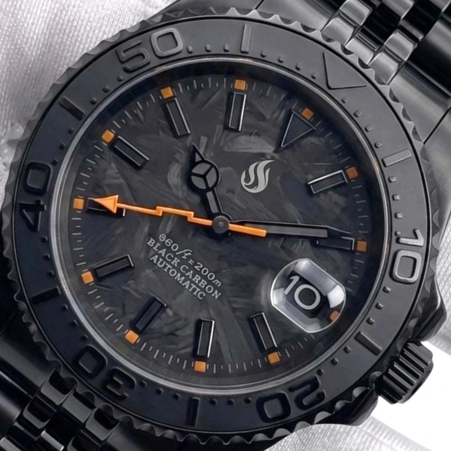 Seiko Mod watches. Close-up of a black automatic Yachtmaster watch with a dark textured dial, black bezel, and orange hour markers and hand, shown on a light fabric background.