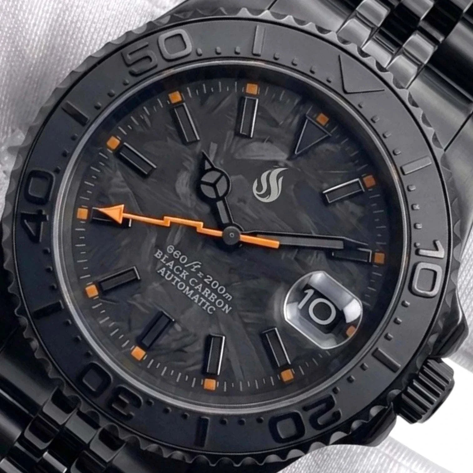 Seiko Mod watches. Close-up of a black automatic Yachtmaster watch with a dark textured dial, black bezel, and orange hour markers and hand, shown on a light fabric background.